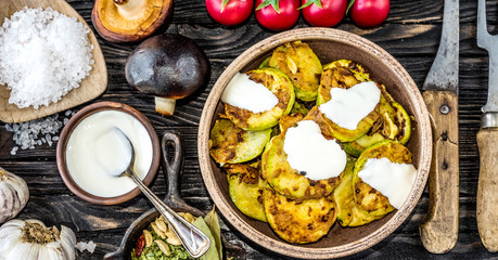 fried zucchini with sour cream and spices on wooden table, top view