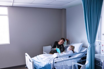Girl on a hospital bed reading book with her father