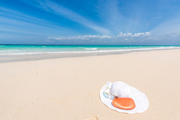 Fototapeta na wymiar white hat, sunglasses and suntan cream on a seashore with blue ocean and sky on the background