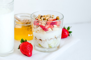 Healthy breakfast of homemade granola cereal with milk, strawberry, nuts and fruit, honey with drizzlier on white background. Morning food, Diet, Detox, Clean Eating, Vegetarian concept.