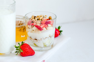 Healthy breakfast of homemade granola cereal with milk, strawberry, nuts and fruit, honey with drizzlier on white background. Morning food, Diet, Detox, Clean Eating, Vegetarian concept.