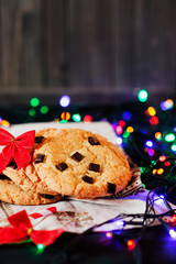 Winter, New Year's atmosphere, American vanilla cookies with chocolate and a glass of milk on a background of colored garlands 