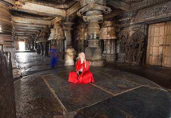 Beautiful woman in traditional indian dress sitting on stone floor of 12th century temple Hoysaleswara, India. Temple was built in 1150 by king of Hoysala Empire, now Karnataka state.