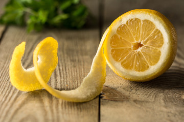 Half peeled fresh lemon on a wooden table with green herbs in the background - 141775012