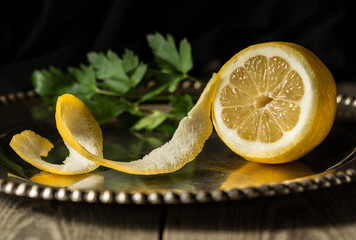 Half peeled fresh lemon on a silver platter with green herbs in the background