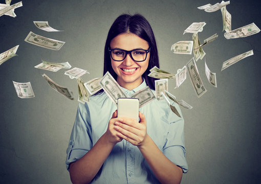 Happy woman in glasses using smartphone with dollar bills flying away