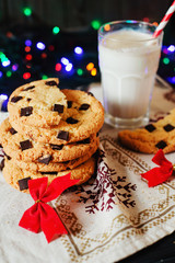 Winter, New Year's atmosphere, American vanilla cookies with chocolate and a glass of milk on a background of colored garlands 
