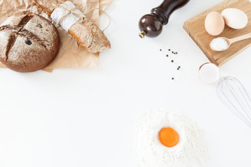 Fototapeta na wymiar Cooking of homemade bread, black round bread and baguette lie on parchment paper on a white background with flour, sliced bread, paper, salt and eggs. Space for text, daylight.