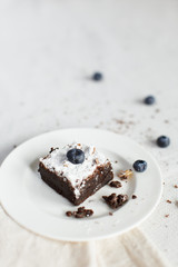 Table setting, chocolate dessert brownie cake on a white plate on a table covered with a linen tablecloth. Vertical shot, daylight.