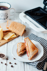 Hearty and traditional breakfast, sandwiches with rye toast, sausage, cheese, spices and black tea on a light wooden background
