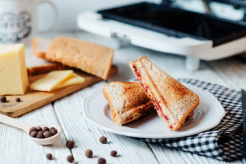 Hearty and traditional breakfast, sandwiches with rye toast, sausage, cheese, spices and black tea on a light wooden background