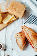 Hearty and traditional breakfast, sandwiches with rye toast, sausage, cheese, spices and black tea on a light wooden background