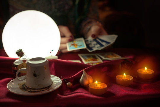 Cofee cup, candles and shiny crystal ball with tarot card in hand of fortune teller woman