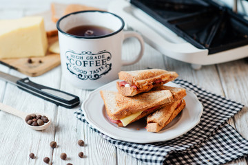 Hearty and traditional breakfast, sandwiches with rye toast, sausage, cheese, spices and black tea on a light wooden background