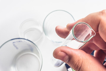 Male hand holds a test tube, against a background of flasks, beakers