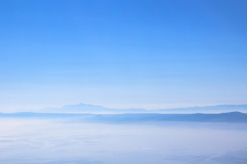 View on island hills and mountains in bright morning mist, fog or clouds above the sea as a minimalistic summer background