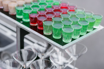 Variety of colorful green red and white beautiful alcohol sweet shooters shots cocktail fresh beverage in small glasses standing in row on mobile bar