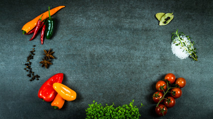 Mix of vegetables, chili, sea salt, pepper, bay leaf, juniper berries, cress, tomatoes and herbs, rosemary and thyme on dark stone background from above with free text space.