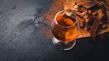 A glass of brandy. Whiskey. Assortment of chocolates. Wooden on the black surface. Top view.