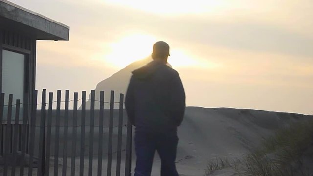 Man walking away near beach house on sandy path to the Pacific Ocean in Oregon's coastline during sunset.