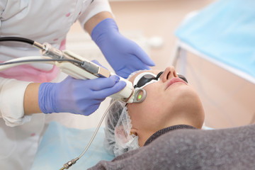 Therapist beautician makes a laser rejuvenation for the Woman by apparatus in a beauty salon.