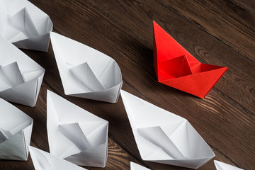 Business leadership concept with white and color paper boats on wooden table