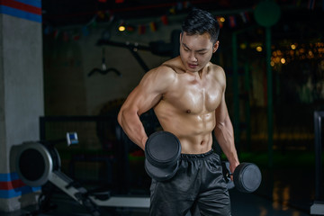 Fototapeta na wymiar Young Chinese athletic man is training in the gym. Makes exercise with the dumbbell