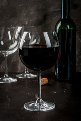 Glass of red wine, with a bottle and empty glasses, on a dark concrete background. Close view copy space