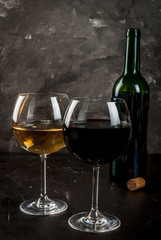 Two glasses of red and white wine, with a bottle, on a dark concrete background. Close view copy space vertical