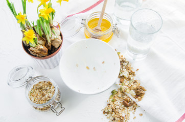 Healthy breakfast fresh granola, muesli in bowl with cereal, nuts, banana fruit, glass of water, bottle, Daffodil flowers. Top view food, Diet, Detox, Clean Eating or Vegetarian.