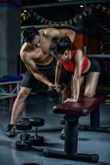 Fototapeta na wymiar Personal Chinese trainer working with his client in gym. Male Chinese personal trainer teaching woman to make right fitness move with the dumbbell.