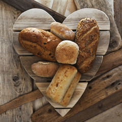 Assorted bread loaves, baps, buns and bakery on wooden heart.