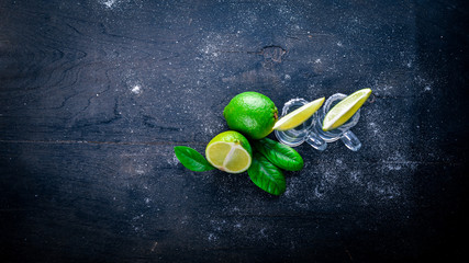 Tequila with lime, lemon, and salt on a black background Wooden. Free space for text . Top view.