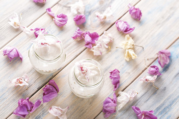 Cream in a jar on a table with flower petals, top view