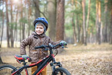 Happy kid boy of 3 or 5 years having fun in autumn forest with a bicycle on beautiful fall day. Active child wearing bike helmet. Safety, sports, leisure with kids concept.