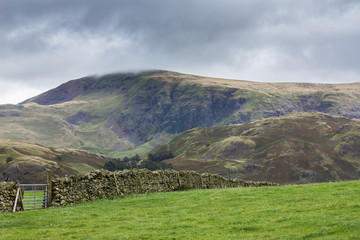 Fototapeta na wymiar Dry Stone Wall among the green fields with mountain in the background in the Lake District