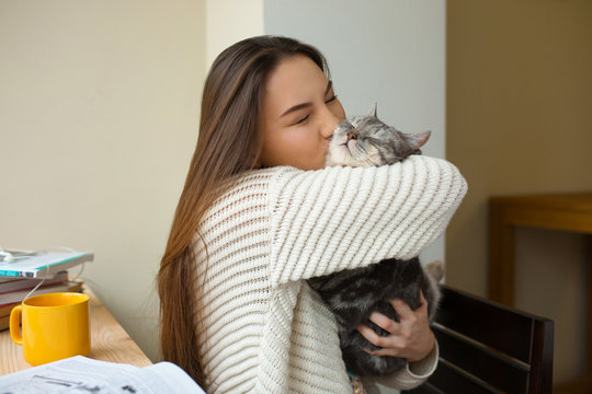 Loving Girl Huging Her Cat At Home Near The Window. Cheerful Girl Kissing Her Pet In A Domestic Clothes. Girl Loves Her Cat. Friends Expressing Feelings