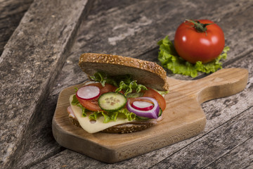 Healthy sandwich made with whole grain bread, lettuce, tomato, radish, cheese and roasted chicken slices.