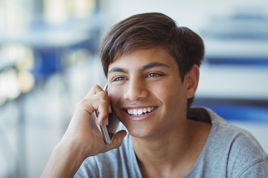 Happy schoolboy talking on mobile phone in classroom - Powered by Adobe