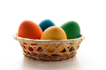 Multicolored easter eggs in a basket, on a white wooden table. The concept of a holiday and a happy Easter. Side view, with space for text. In a high key