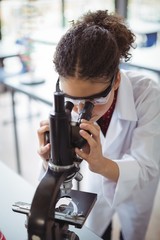 Attentive schoolgirl looking through microscope in laboratory
