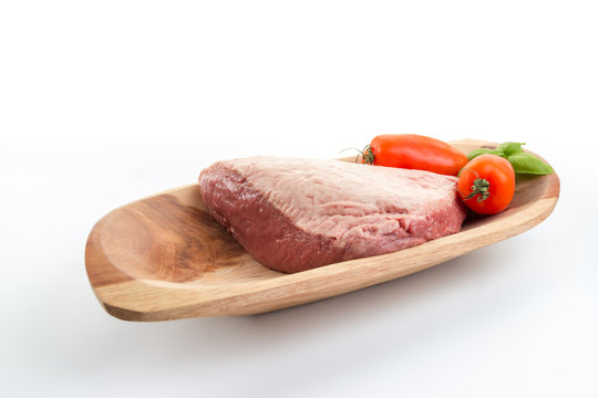 Full piece of raw cow beef (picanha), tomatoes and basil on a wood rectangular bow - white background