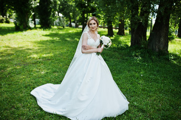 Cute blonde bride with wedding bouquet at park on sunny day.