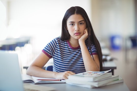 Portrait of sad schoolgirl sitting in classroom - Powered by Adobe