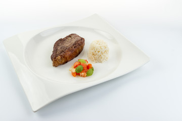 Slice of barbecued cow beef (picanha) with rice, tomato salad and basil leaves on a white dish with white background