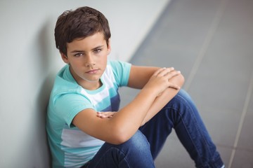 Portrait of sad schoolboy sitting in corridor