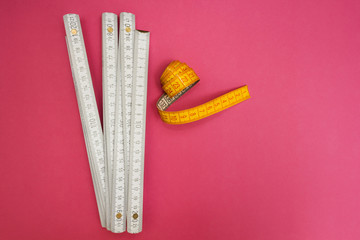 Folding ruler and measuring tape on a pink background.
