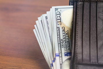 Wallet with hundred dollar banknotes on wooden background, money and finance concept.