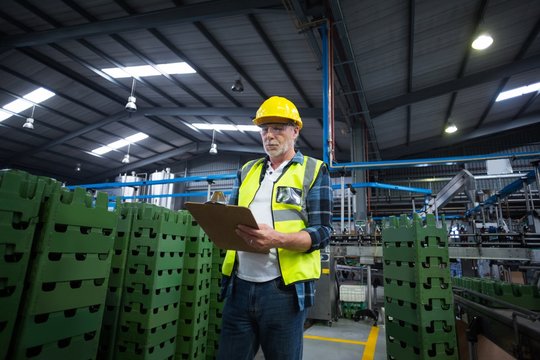 Male factory worker maintaining record on clipboard