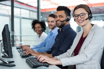 Naklejka premium Business executives with headsets using computers at desk in office